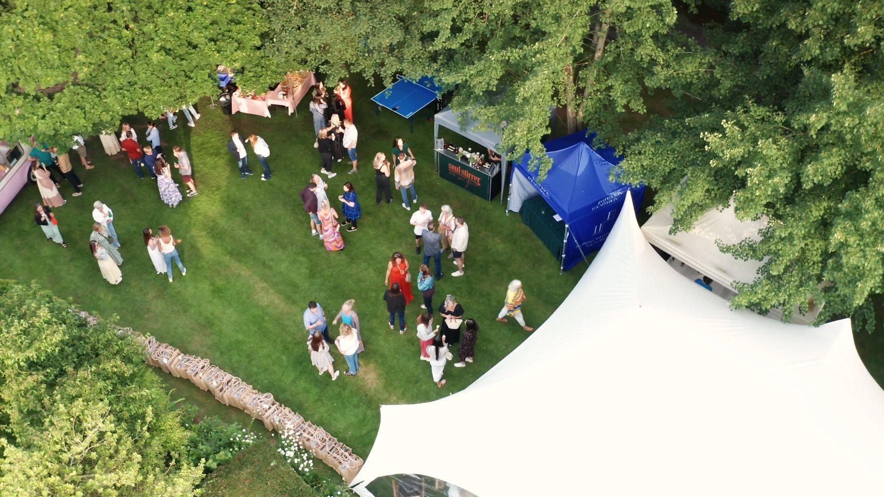 The summer party on the manor lawn, seen from above, with a white marquee