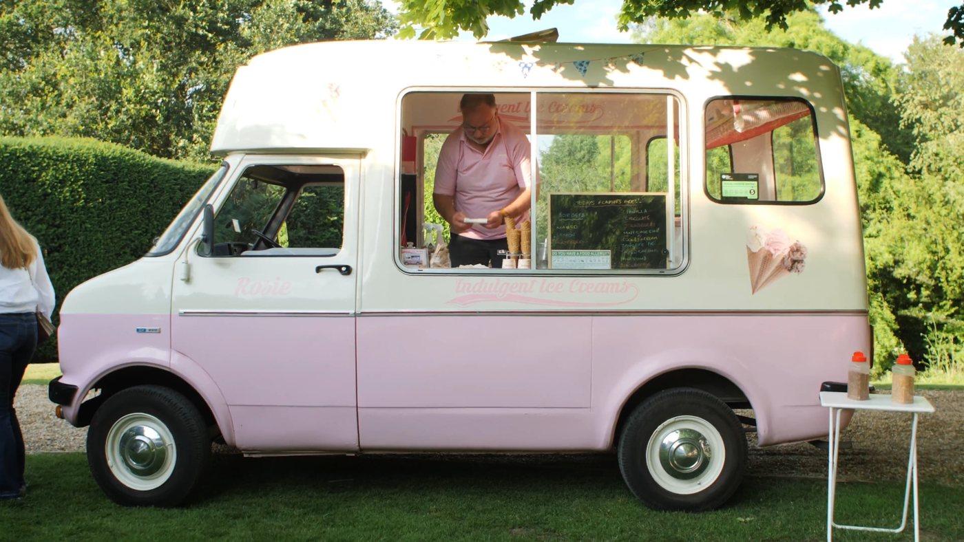 A pink and cream ice-cream van parked on the grass